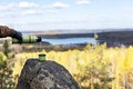 Male hands in warm gloves pour hot tea from thermos on rock against the backdrop of beautiful autumn view of lake and forest with Royalty Free Stock Photo