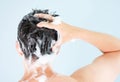 Male hands wash their hair with shampoo and foam on gray background, rear view. Royalty Free Stock Photo