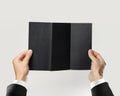 Male hands in white shirt and black jacket holding a black booklet triple sheet of paper. Isolated on gray background. Closeup