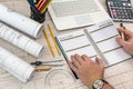 Male hands writing on notepad with part of industrial blueprint with calculator, tools and laptop Royalty Free Stock Photo