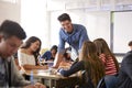 Male High School Teacher Standing By Student Table Teaching Lesson