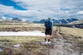 Male hiker with backpack standing on gravel path looking towards snow covered peaks during spring.