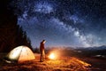 Male hiker have a rest in his camp near the forest at night under beautiful night sky full of stars and milky way Royalty Free Stock Photo