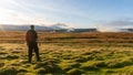 A male hiker looking out across a bleak moorland as the sun sets. With clouds covering hills in the distance. Brecon Beacons