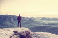 Male hiker stand on edge and enjoying dramatic overlook of misty landscape. The Sun is hidden in thick mist and change colors Royalty Free Stock Photo