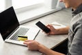 male holding credit card typing numbers on computer keyboard while sitting at home at the wooden table, flare sun light