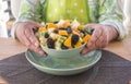 A male holding a green plate filled with a fresh fruit salad. One senior people. Wooden table