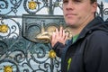 A male holding his hand against a decorative bronze plaque on a fence in Prague.