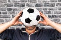 Male holding a soccer ball in front of his face against a grey cobblestone wall