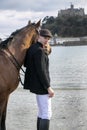 Handsome man, Male Horse Rider walking with his horse on beach, wearing traditional flat cap, white trousers, red polo shirt Royalty Free Stock Photo