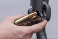 A male hunter loads cartridges for a rifle magazine on a light background, equip a combat weapon.