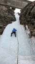 Male ice climber in a blue jacket climbs a frozen waterfall in the Avers Valley in the Swiss Alps