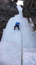 Male ice climber in a blue jacket climbs a frozen waterfall in the Avers Valley in the Swiss Alps