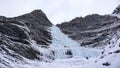 Male ice climber stands at the headwall of a long and steep waterfall in the Alps