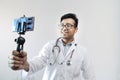 Male indian doctor in white coat and stethoscope clicking selfie with a mobile tripod and futuristic concept cameraphone Royalty Free Stock Photo