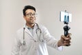 Male indian doctor in white coat and stethoscope clicking selfie with a mobile tripod and futuristic concept cameraphone Royalty Free Stock Photo