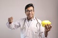 Male indian doctor in white coat and stethoscope with a yellow piggy bank showing money sign Royalty Free Stock Photo