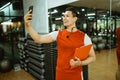 male instructor standing holding clipboard making video call with smartphone