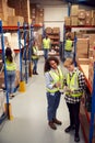 Male Intern With Team Leader Looking At Clipboard Inside Busy Warehouse Facility Royalty Free Stock Photo