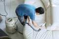 Male janitor cleans couch with a vacuum cleaner