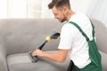 Male janitor removing dirt from sofa with cleaner