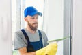 Male janitor using a squeegee to clean a window in an office wearing an apron and gloves as he works Royalty Free Stock Photo