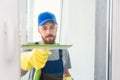 Male janitor using a squeegee to clean a window in an office wearing an apron and gloves as he works Royalty Free Stock Photo