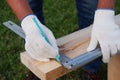 A male joiner marks a right angle on a wooden board with a square. Worker on the lawn near the house. Close-up view of the tool. Royalty Free Stock Photo