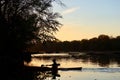 Male kayaker paddling across a lake against sunset