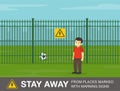 Male kid stands next to the green fence. Stay away from places marked with warning signs.