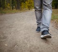 Male legs in jeans and sneakers walking out into the distance on the ground covered with fallen yellow leaves. Autumn arrival Royalty Free Stock Photo