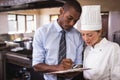 Male manager and female chef writing on clipboard in kitchen Royalty Free Stock Photo