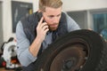 male mechanic looking at wheel and talking on smartphone Royalty Free Stock Photo