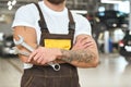 Male mechanic with muscular hands and tattoo keeping wrench