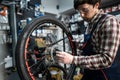 Male mechanic working in bicycle repair shop, mechanic repairing bike using special tool, wearing protective gloves. Young