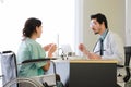 Male medical practitioner in uniform explaining how to eat pills to woman on wheelchair during appointment in modern hospital