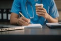 Male medicine doctor, physician or practitioner in lab room writing on blank notebook and work on laptop computer with medical Royalty Free Stock Photo