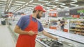 Male merchandiser in red uniform checking products with digital tablet