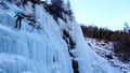 Male mountain guide climbing a steep frozen waterfall on a cold winter day in the Alps