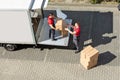 Male Movers Unloading The Cardboard Boxes Form Truck