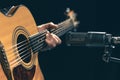 Male musician playing acoustic guitar behind microphone in recording studio. Royalty Free Stock Photo