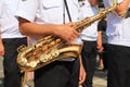 A male musician in a white shirt holds a large beautiful golden saxophone in a column of military musicians, close-up