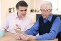 Male Neighbor Showing Senior Man How To Use Digital Tablet
