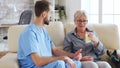 Male nurse sitting on couch with senior woman giving her medical treatment in nursing home Royalty Free Stock Photo