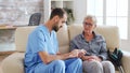 Male nurse sitting on couch with senior woman giving her medical treatment in nursing home Royalty Free Stock Photo