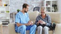 Male nurse sitting on couch with senior woman giving her medical treatment in nursing home Royalty Free Stock Photo