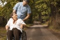 Nurse supporting smiling senior woman in the wheelchair while walking in the forest