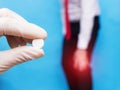 Male office worker holds sore knee joint, pain and inflammation in knee, doctor holds pill, blue background, arthrosis