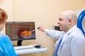 A male ophthalmologist explains the results of an eye examination to an adult woman, showing a drawing on a computer