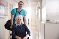 Male Orderly Pushing Senior Female Patient Being Discharged From Hospital In Wheelchair